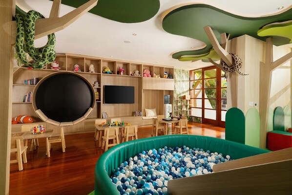 Una sala de juegos infantil con piscina de pelotas, estanterías de madera con juguetes, un televisor de pantalla plana grande y un diseño de techo verde.