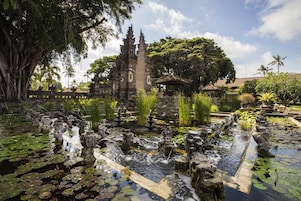 A traditional temple with intricate carvings, a pond with statues, and lush greenery.