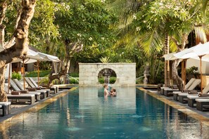 A pool area with lounge chairs and umbrellas, surrounded by lush greenery and a stone archway. - Nusa Dua Beach Hotel and Spa - Handwritten Collection (Nusa Dua)