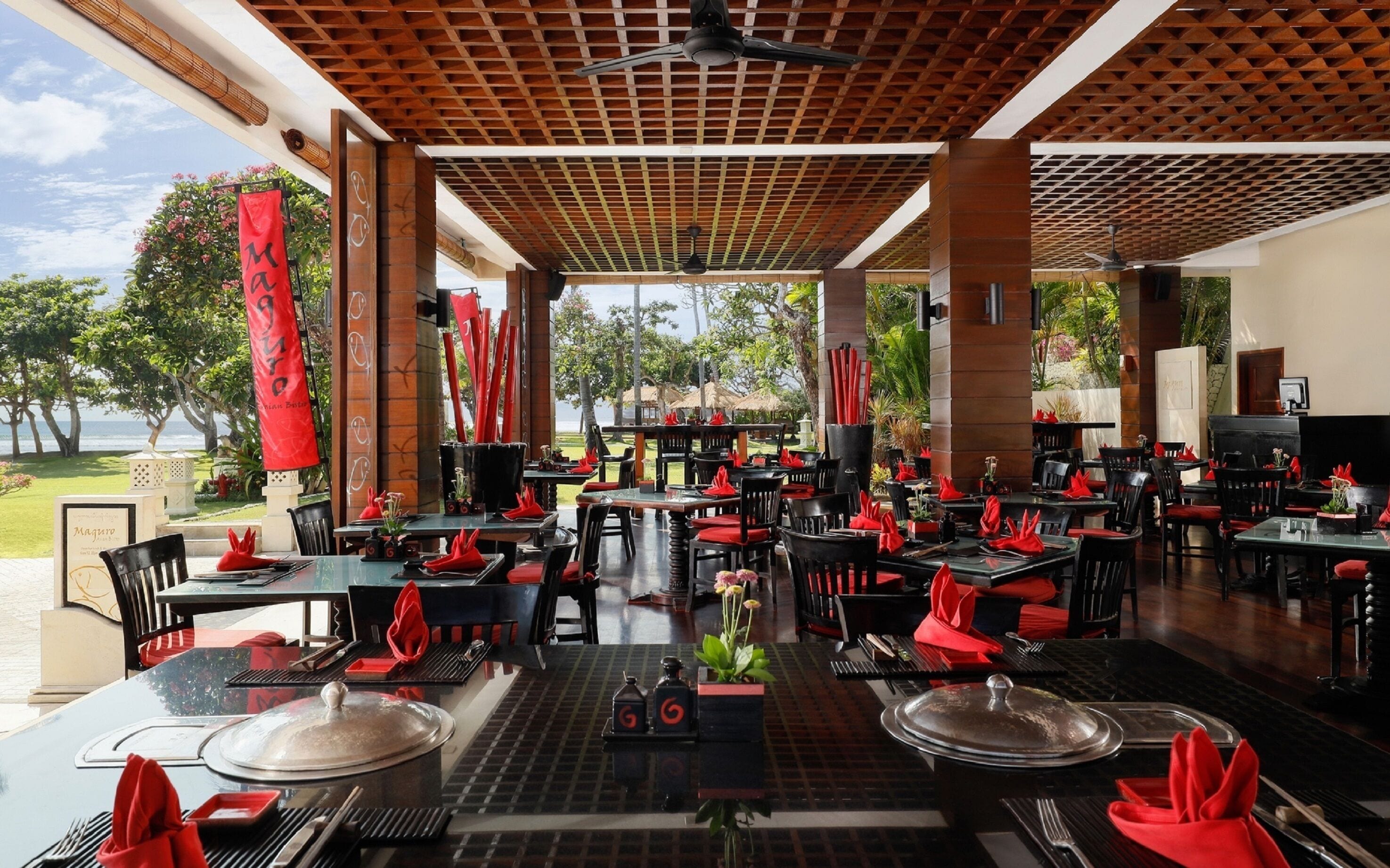 A restaurant with outdoor seating, red napkins, and a view of the ocean.