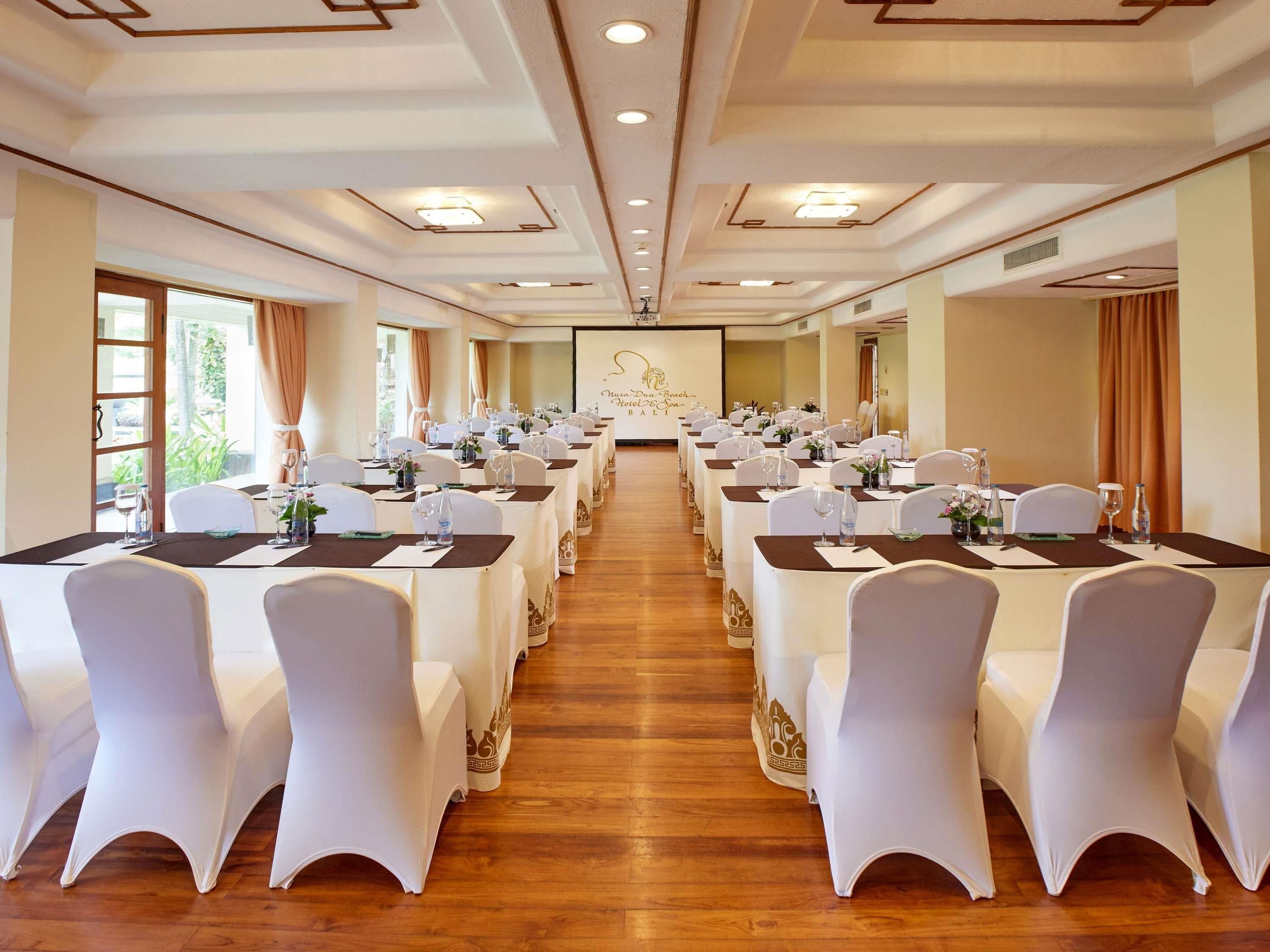 A conference room with rows of tables and chairs, equipped with water bottles and glassware.