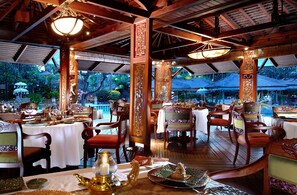 An outdoor restaurant with wooden tables and chairs, covered with white tablecloths, and ornate pillars.