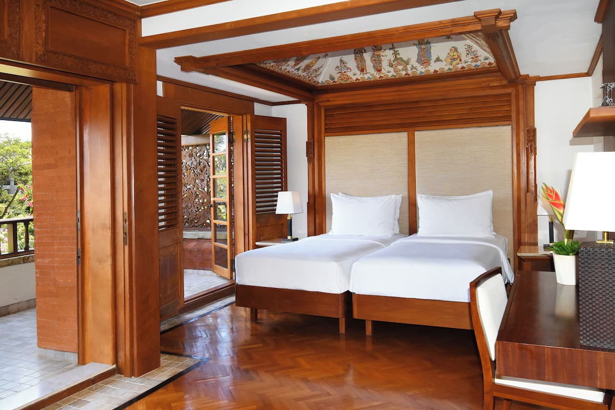 A double bed with a wooden headboard, a bedside table with a lamp, and a view of a balcony with wooden railings.