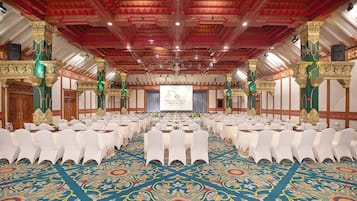 A large conference room with rows of white chairs, a stage with a screen, and ornate columns.