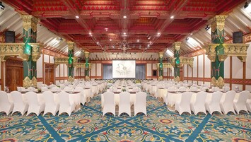 A large conference room with rows of white chairs, a stage with a screen, and ornate columns.