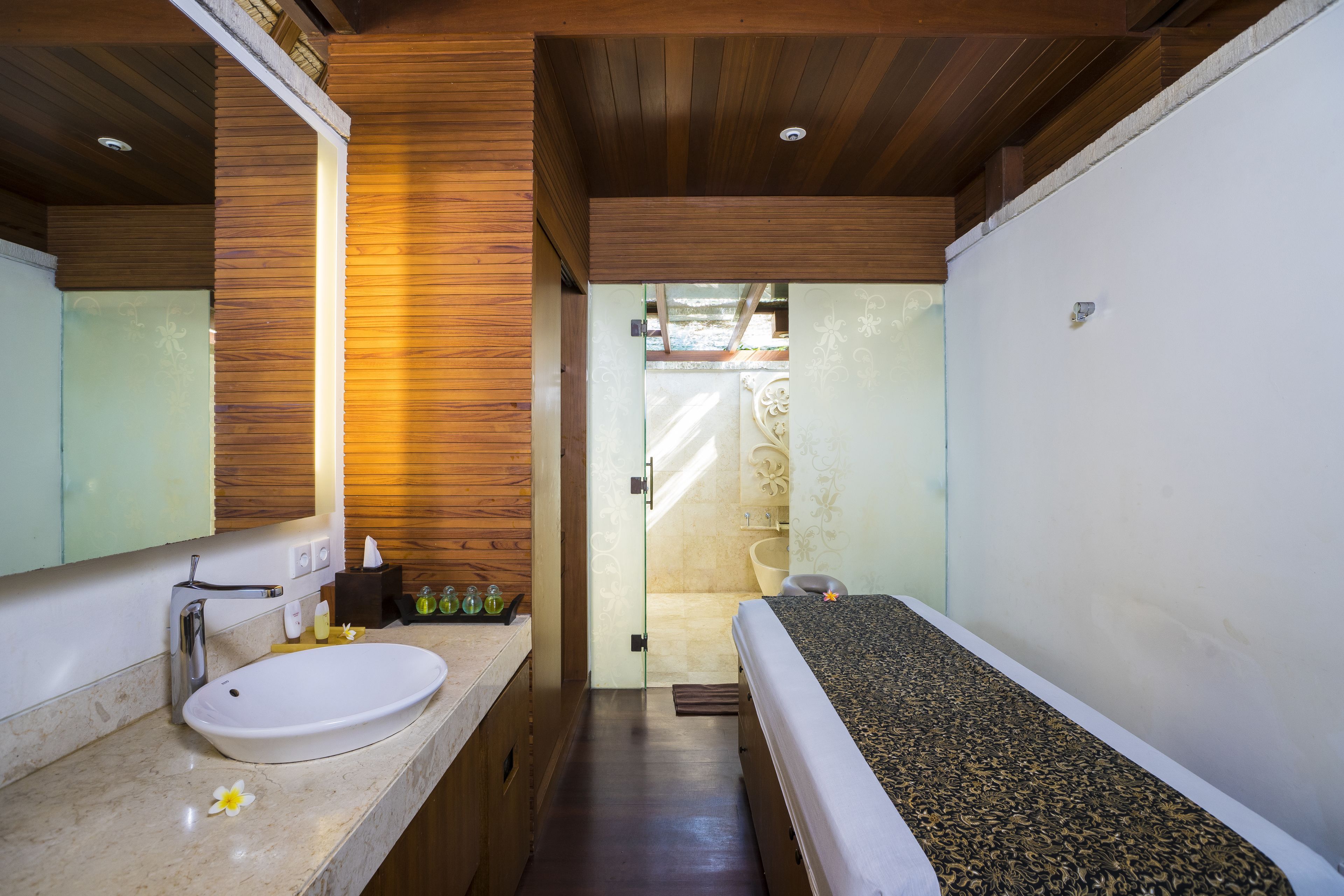 A bathroom with a wooden ceiling, a white sink, and a bed with a patterned headboard.
