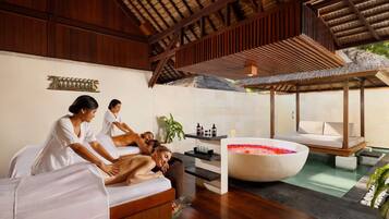A spa area with wooden beams, a large bathtub with rose petals, and a massage table.
