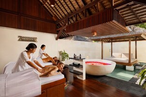 A spa area with wooden beams, a large bathtub with rose petals, and a massage table.