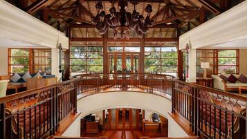 A spacious interior with a central staircase, wooden railings, and large windows offering a view of greenery outside.