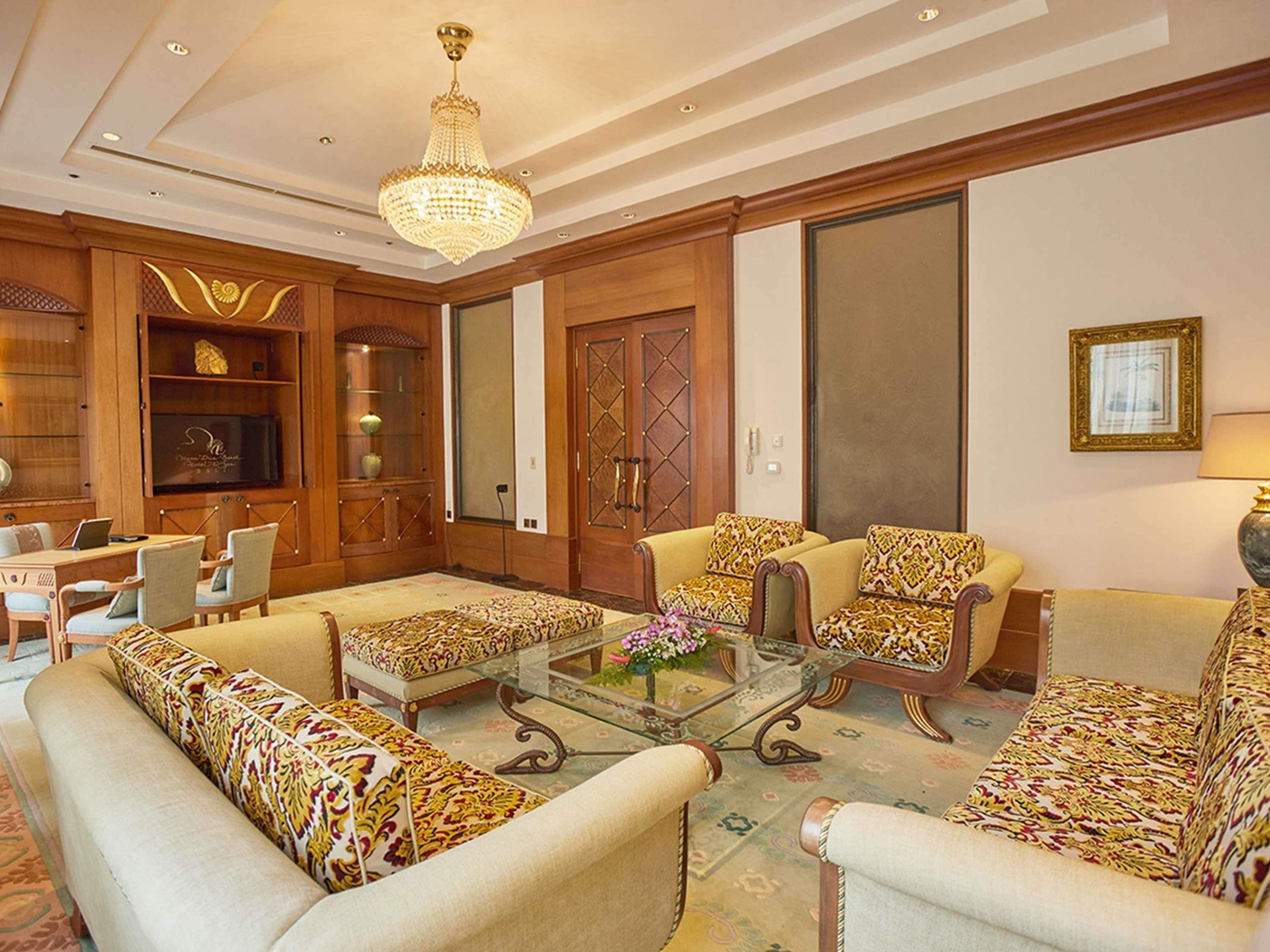 A spacious living room with a chandelier, patterned sofas, a glass coffee table, and wooden paneling.