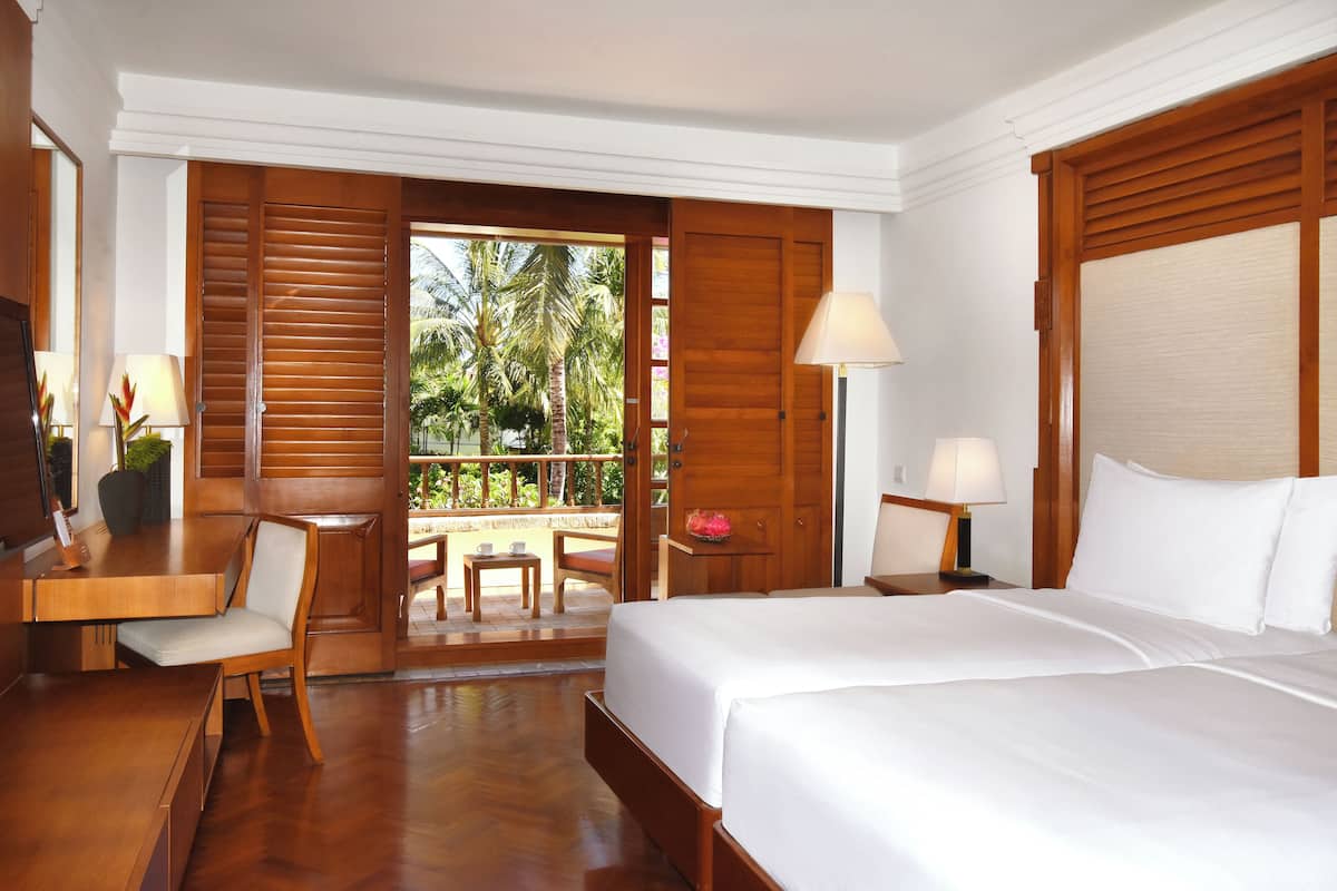 A hotel room with a bed, a desk, a chair, a table, and a view of palm trees.