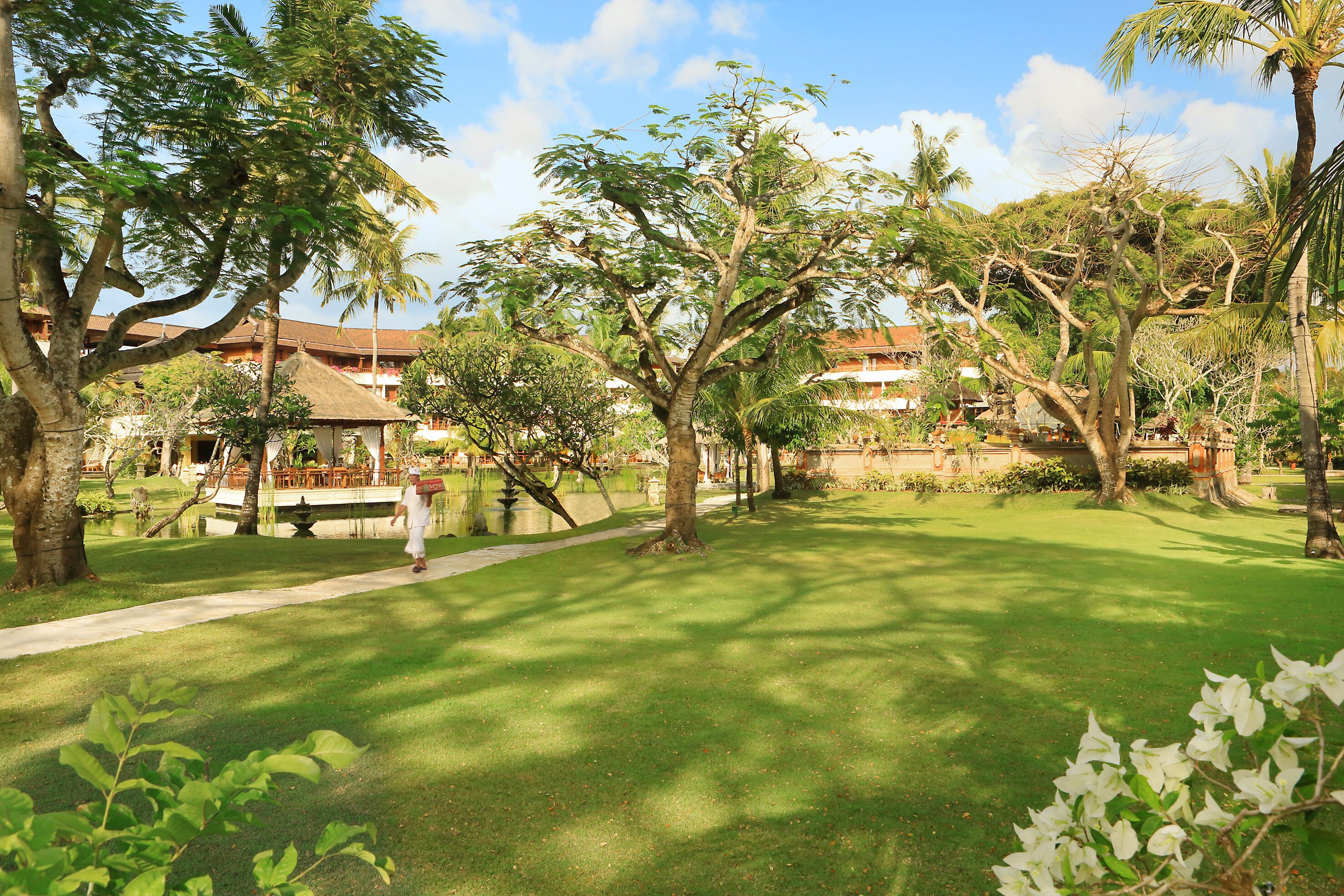 A well-maintained garden with a pathway, palm trees, and a building in the background.
