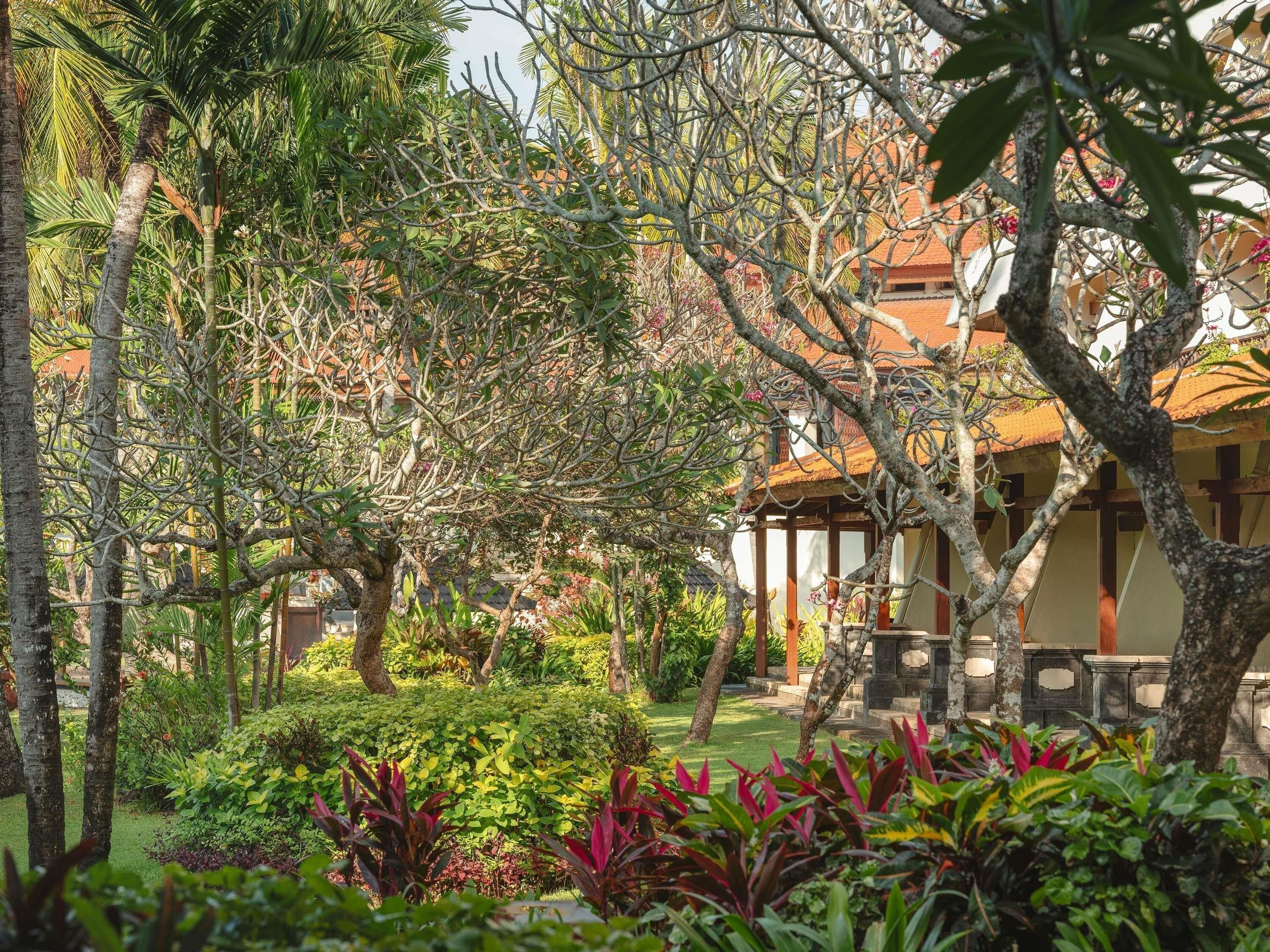 A lush garden with various plants and trees, a gazebo, and a building with a tiled roof.