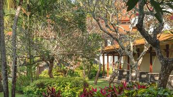 A lush garden with various plants and trees, a gazebo, and a building with a tiled roof.
