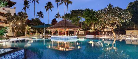 A pool area with a gazebo, palm trees, and a traditional building.