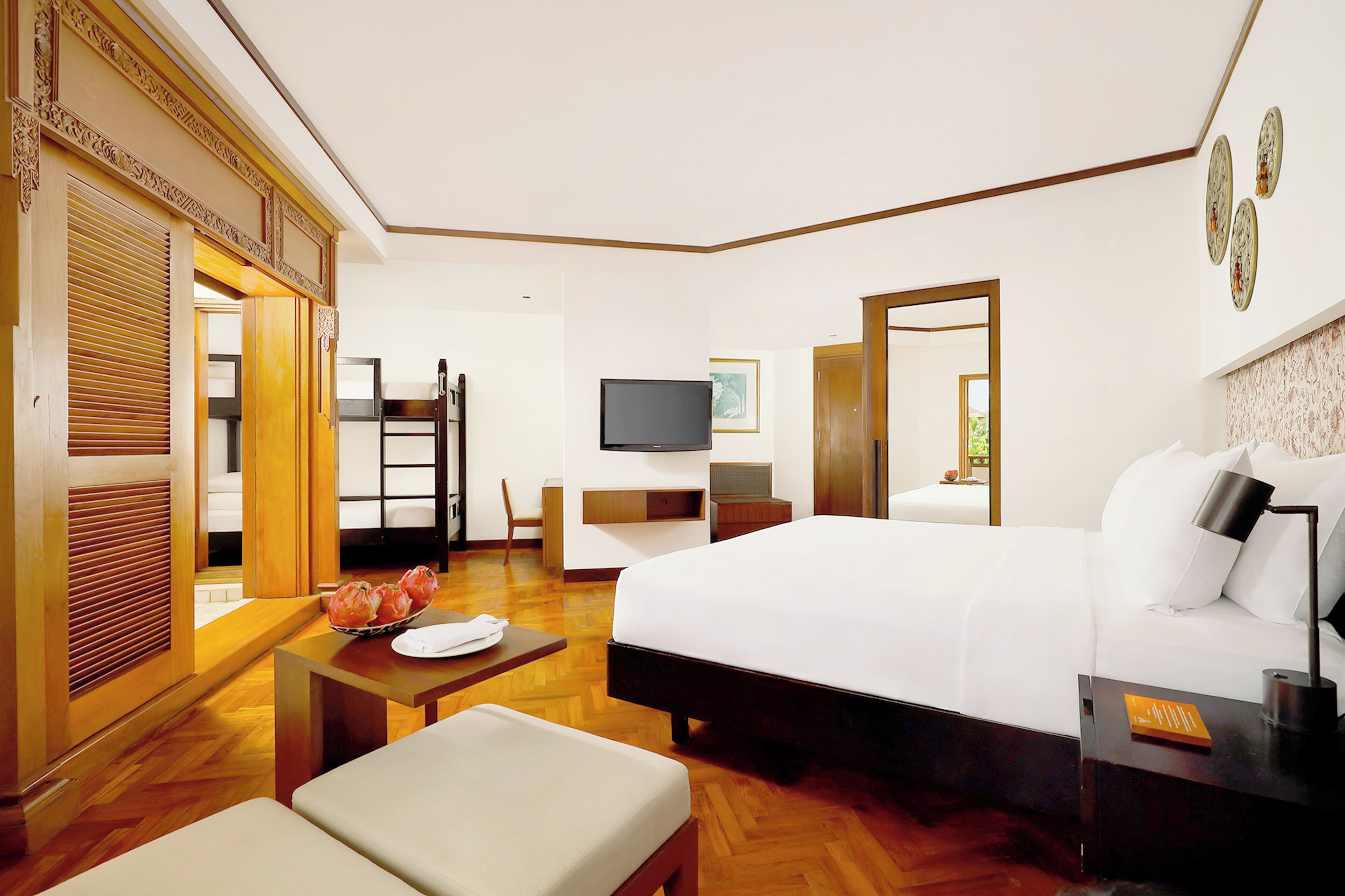 Habitación de hotel con una cama grande, un escritorio con televisor de pantalla plana, una mesa de comedor con frutero, un sofá y un espejo.