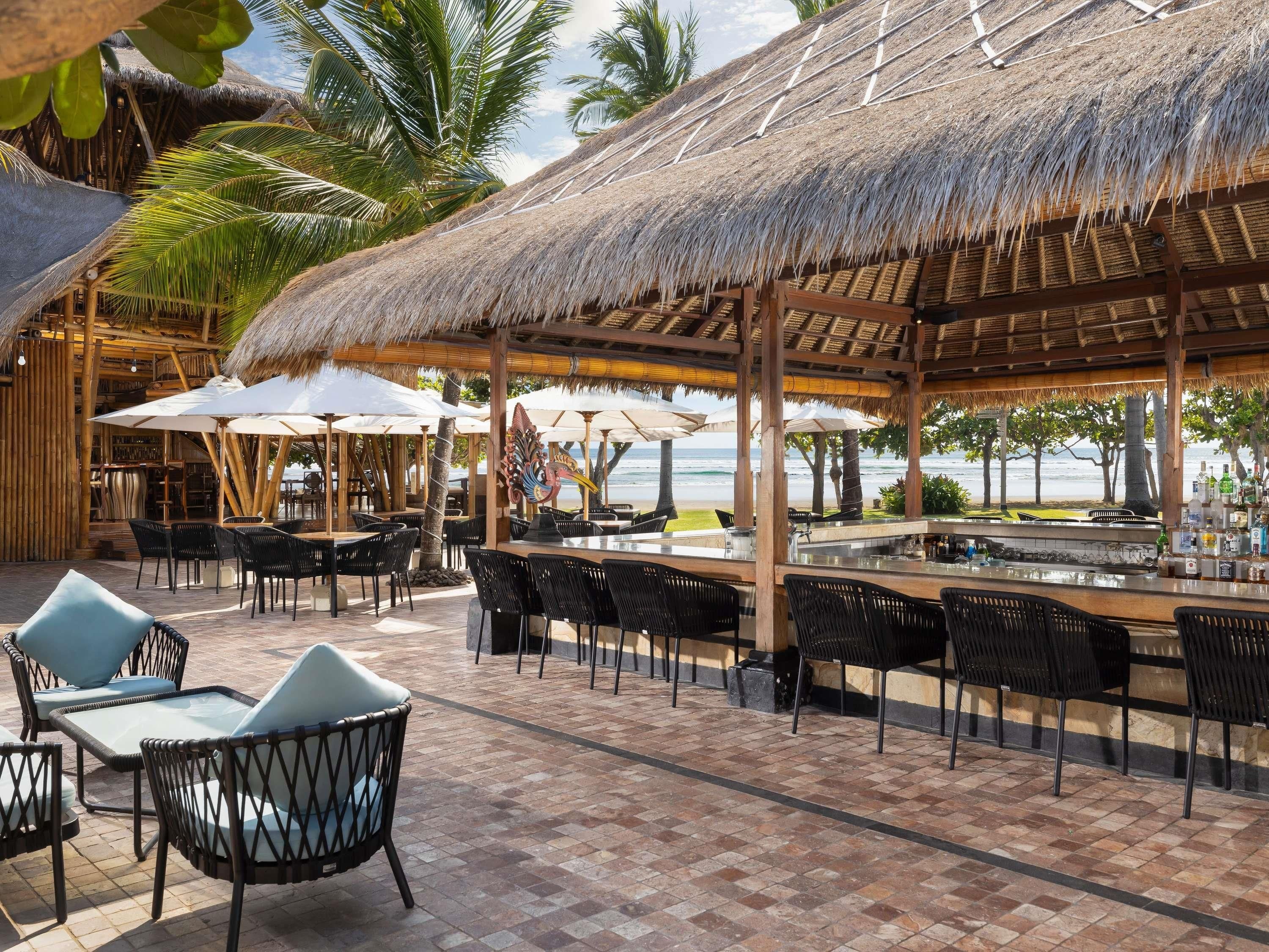 An outdoor bar area with thatched roofs, black wicker furniture, and a view of the sea.