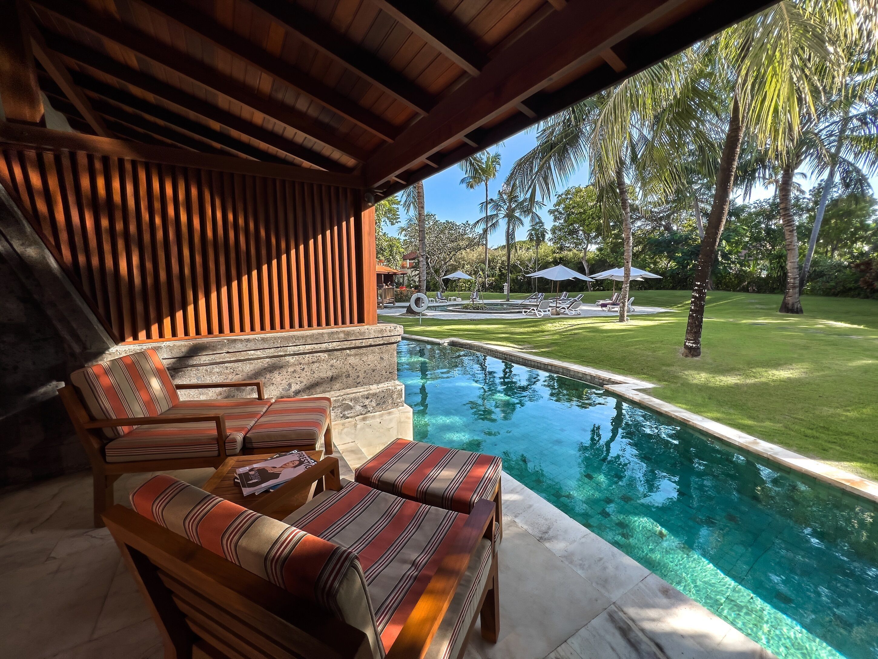 A poolside area with wooden furniture and a view of the pool and surrounding greenery.
