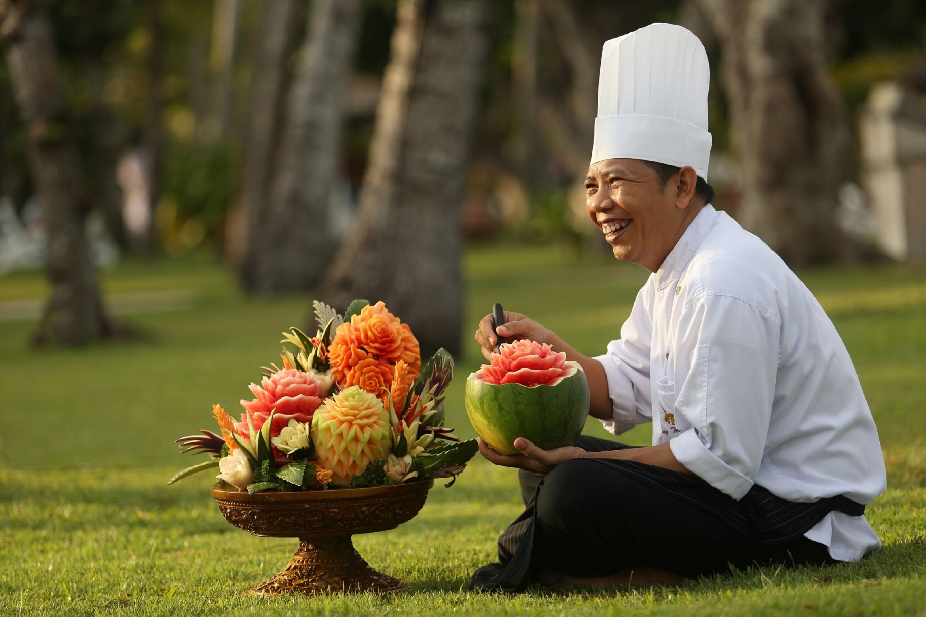 Un chef corta una sandía al aire libre, cerca hay un arreglo floral.