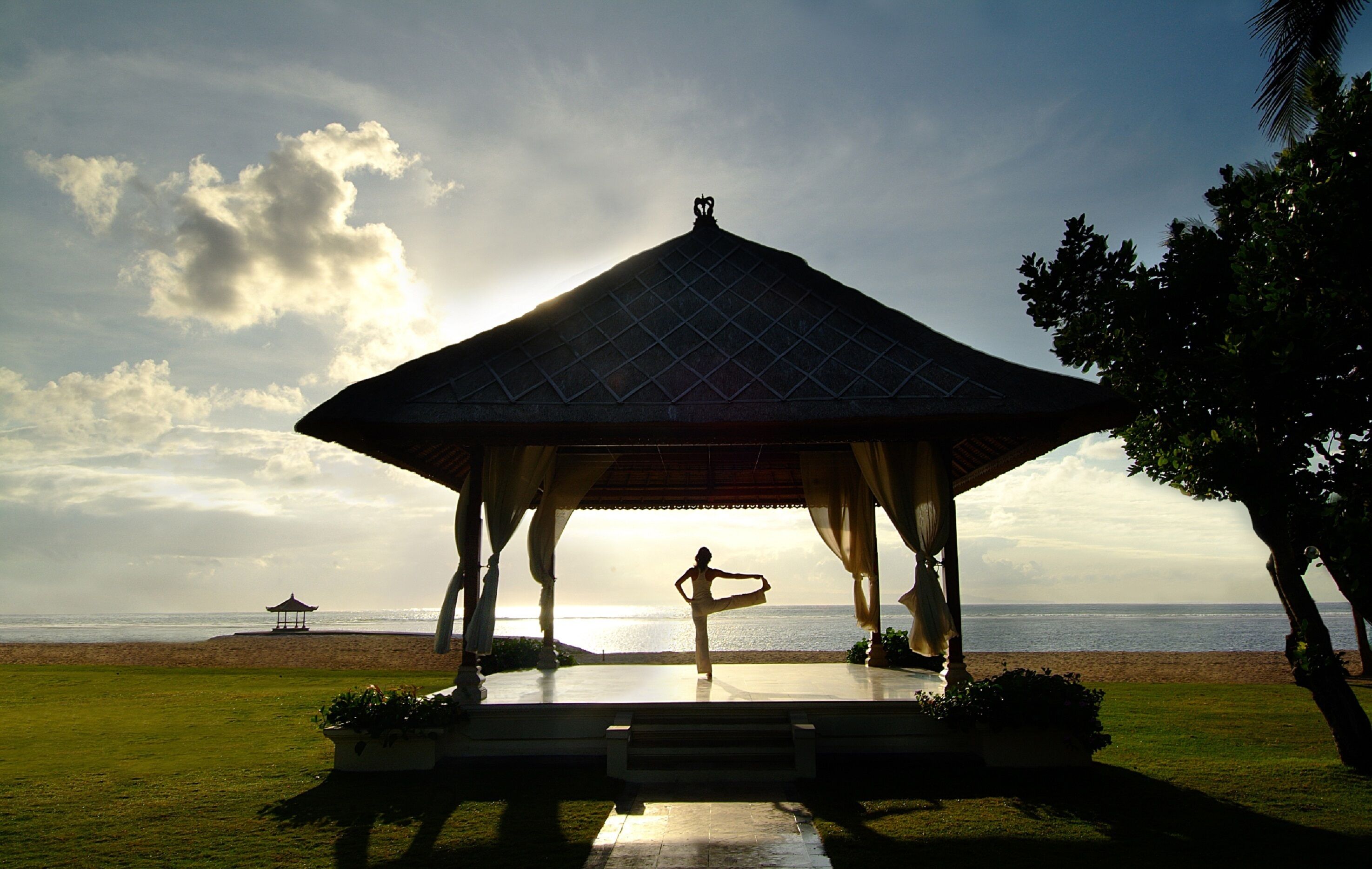A gazebo with a view of the sea, a person performing yoga, and a distant pagoda.
