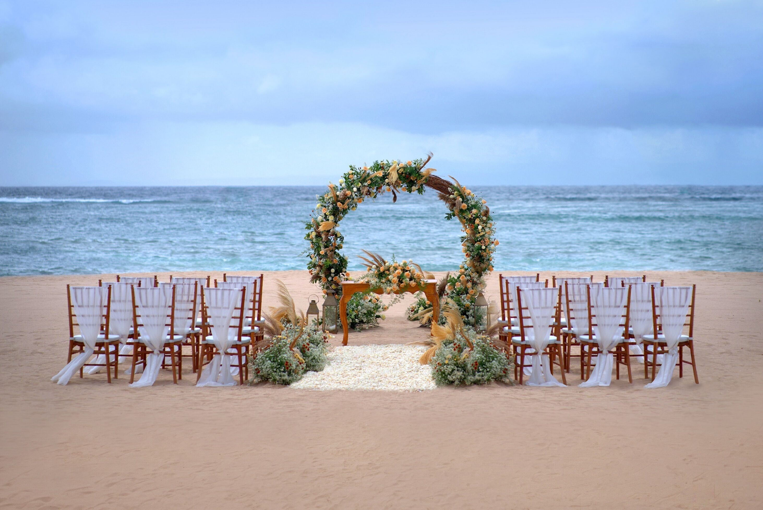 A beach wedding setup with a floral arch and chairs arranged for guests.