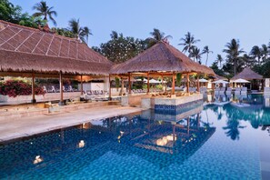 A pool area with thatched-roof structures, lounge chairs, and a clear blue pool. - Nusa Dua Beach Hotel and Spa - Handwritten Collection (Nusa Dua)