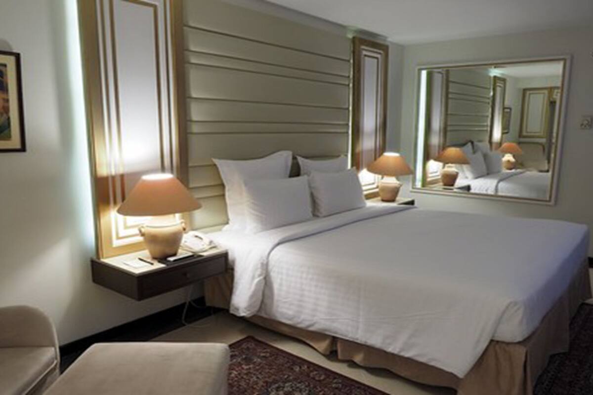 Une chambre d’hôtel avec un grand lit, deux tables de chevet avec des lampes, un miroir et un sol recouvert de moquette.