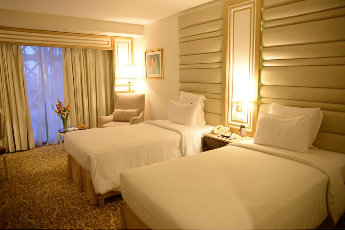 Une chambre d’hôtel avec deux lits, un coin salon, un bureau et une fenêtre avec des rideaux.