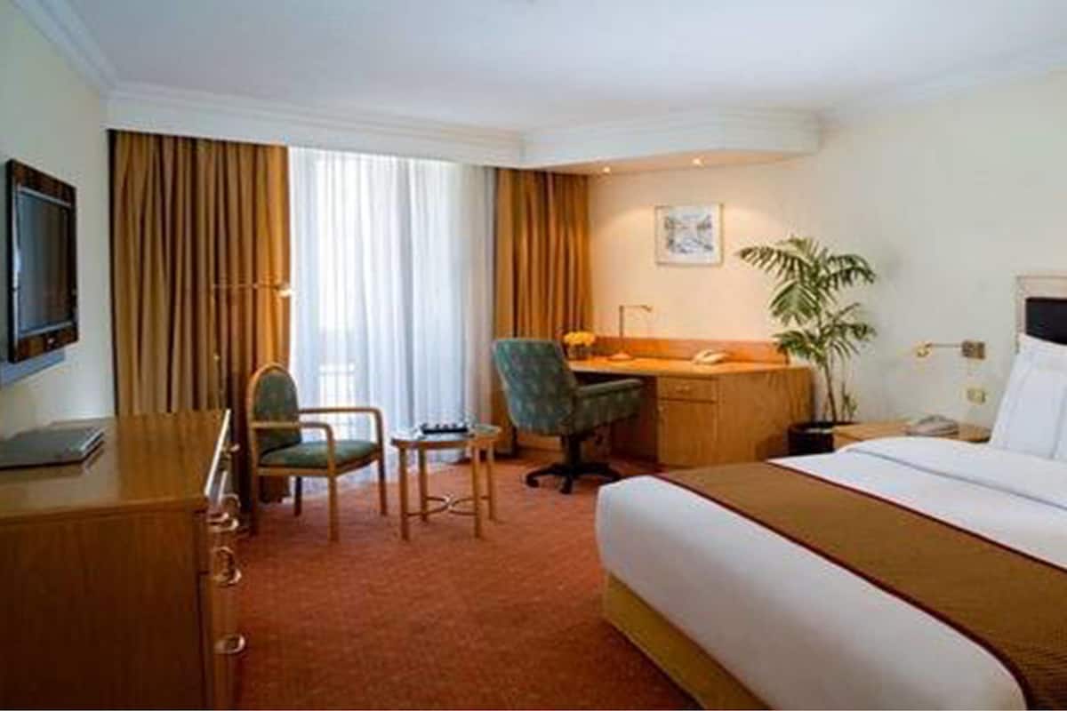 Une chambre d’hôtel équipée d’un lit, d’un bureau, d’une chaise, d’une télévision et d’une plante.