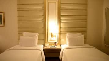 A hotel room with two single beds, a nightstand with a lamp, and a mirror above the bed.