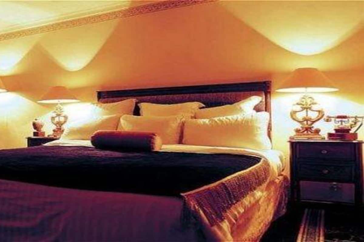 Un lit bien fait, avec des oreillers et une couverture, une table de chevet avec une lampe, et une petite table de nuit également avec une lampe.