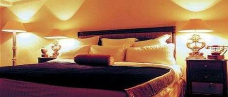 Een netjes opgemaakt bed met kussens en dekbed, een nachtkastje met een lamp.