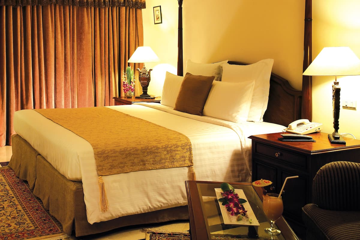 Une chambre d’hôtel avec un grand lit, deux tables de chevet, une petite table, un bureau avec une lampe et une chaise.
