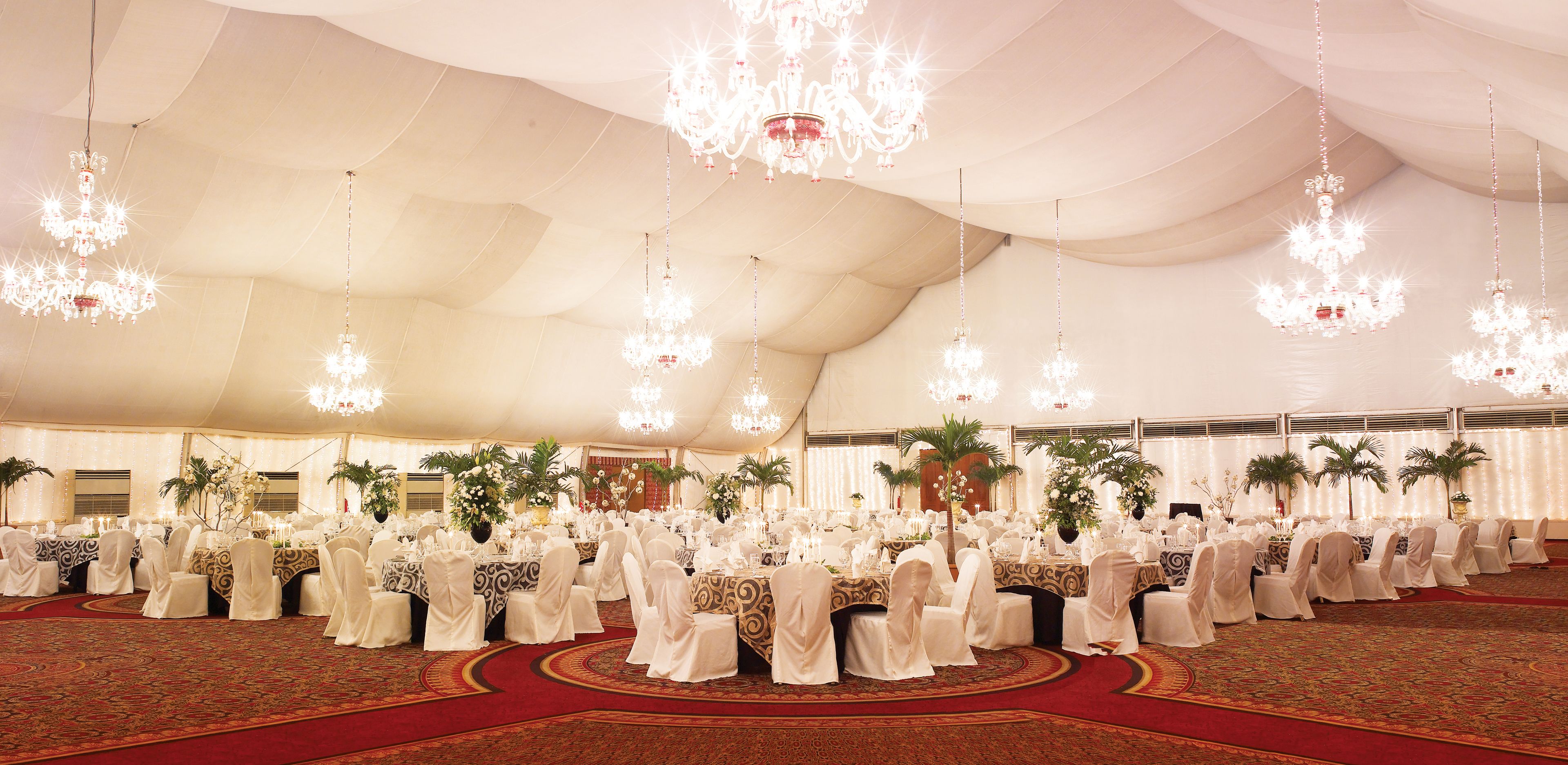 A tented event space with round tables, white tablecloths, and chandeliers.