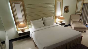 Habitación de hotel con una cama grande, dos mesitas de noche, una silla y una mesita con lámpara.