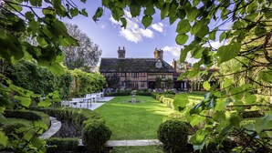 A traditional Tudor-style building with a well-manicured garden, a fountain, and a seating area. - Langshott Manor (Horley)