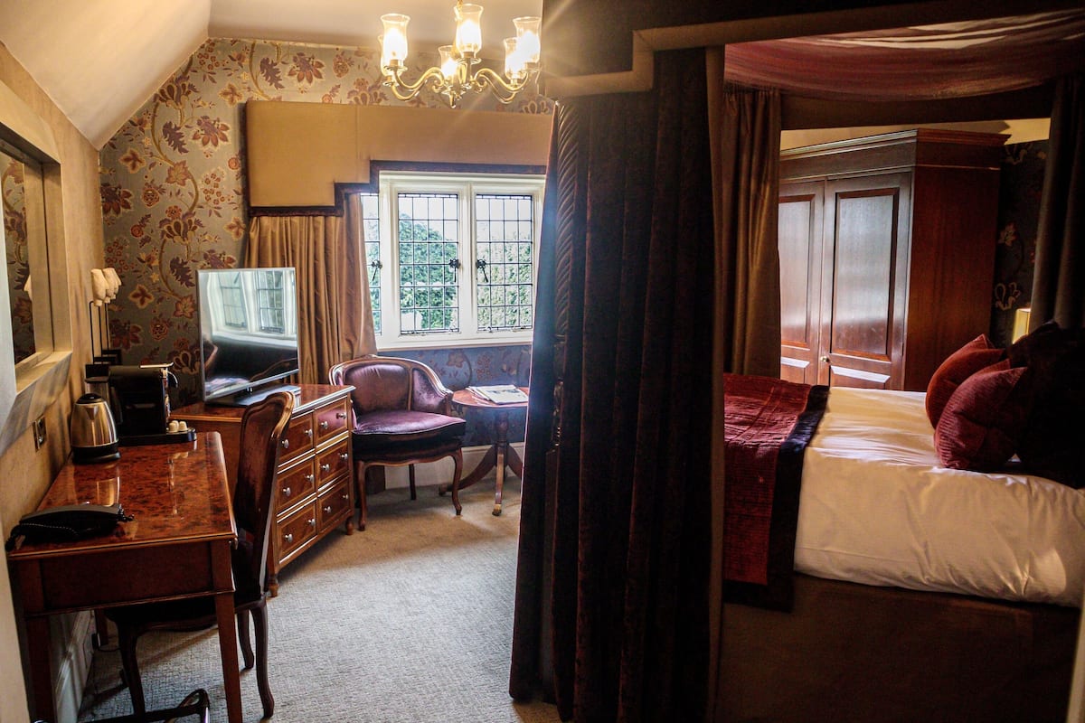 A hotel room with a bed, a desk with a chair, a television, and a window with curtains.