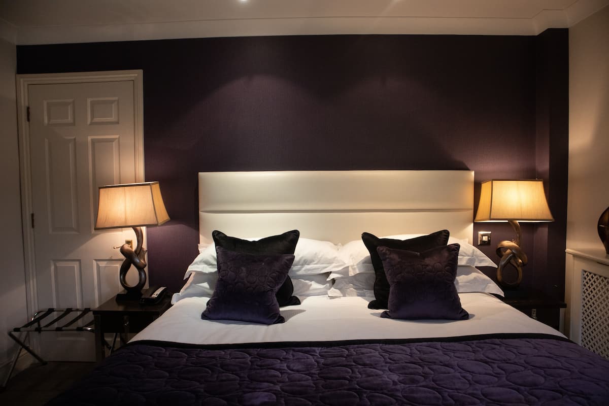 A neatly made bed with two decorative pillows, two bedside lamps, and a white door in a hotel room.