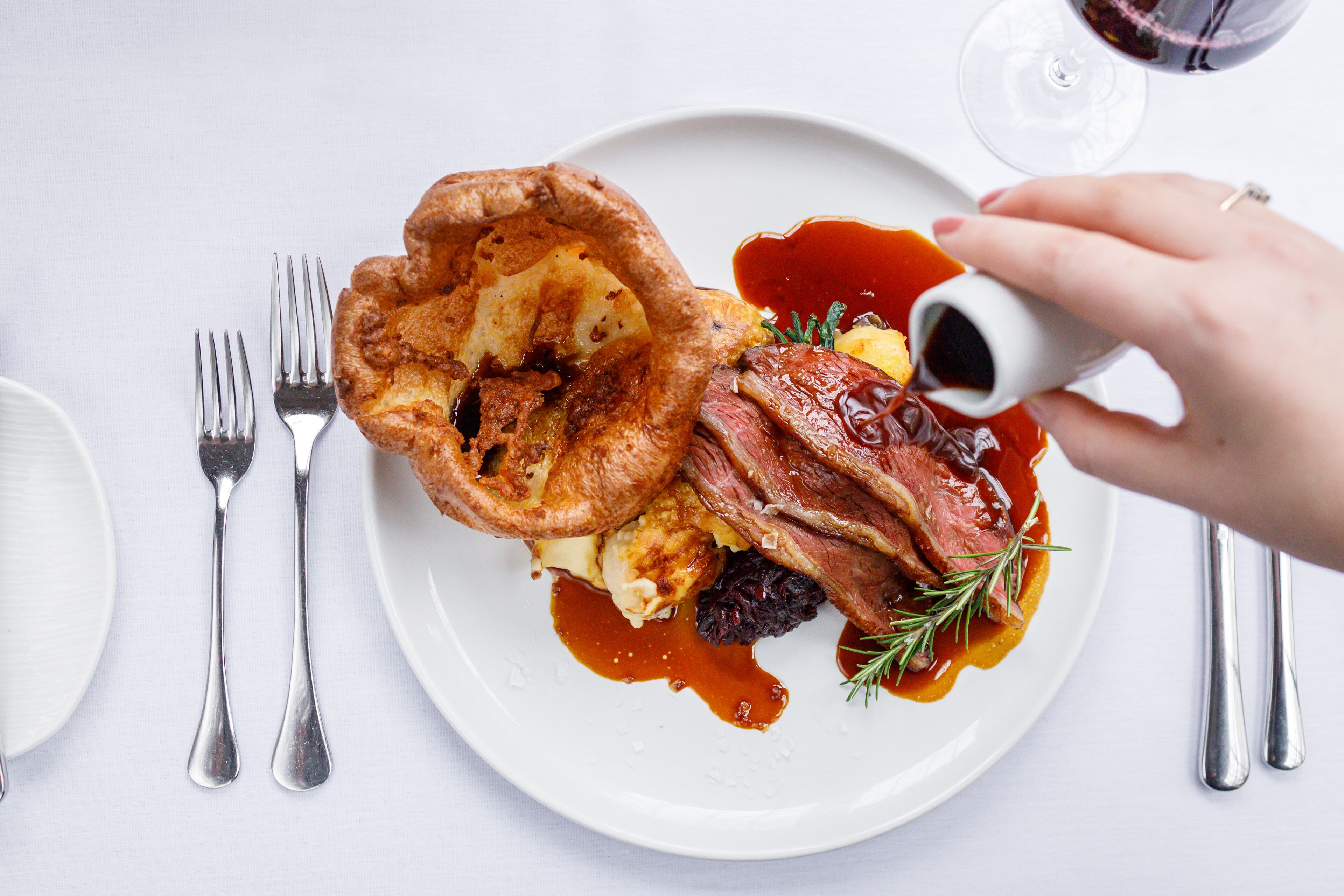 A plate with Yorkshire pudding, meat, and vegetables, accompanied by a glass of red wine.