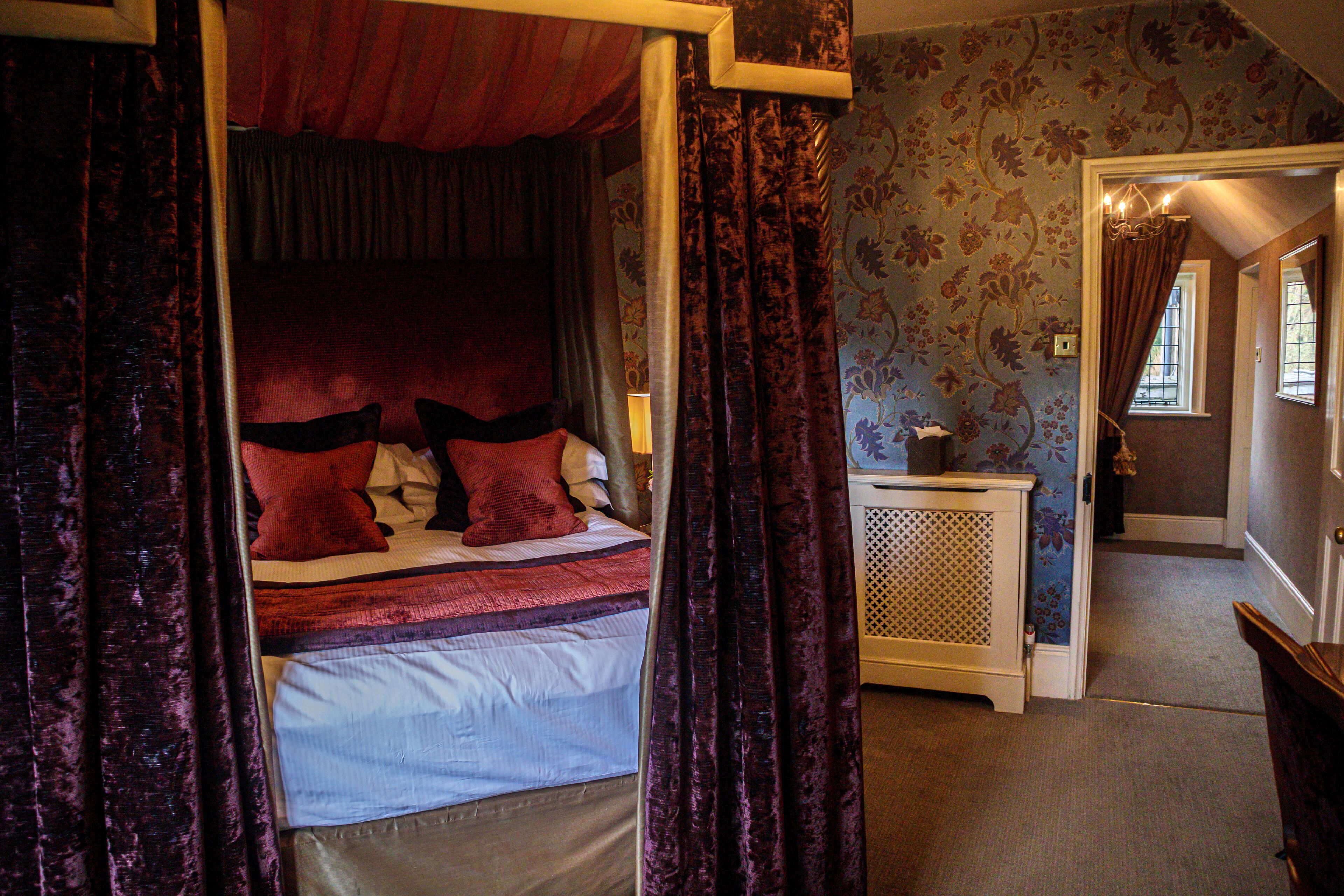 A bedroom with a canopy bed, a nightstand, and a door leading to another room.