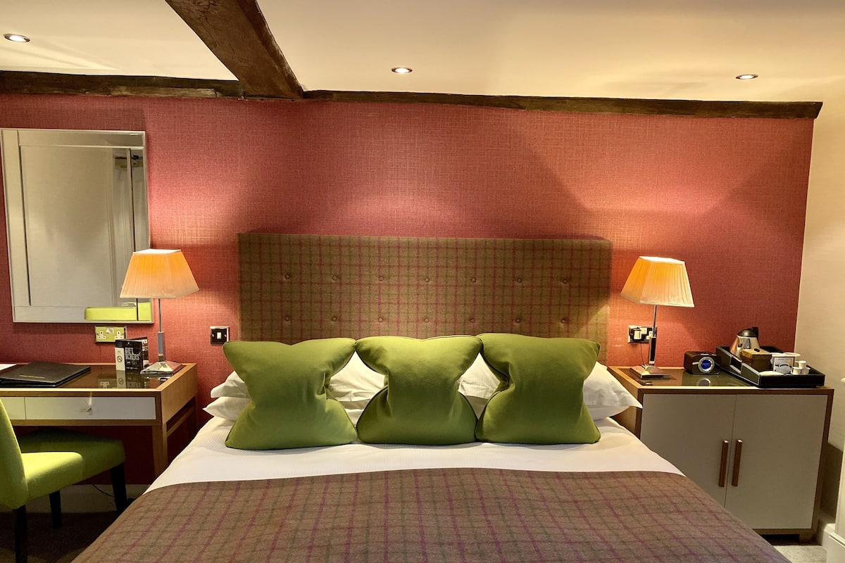 A hotel room with a bed, two bedside lamps, a desk with a chair, a mirror, and a wardrobe.