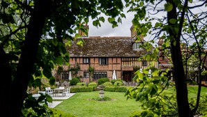 A traditional Tudor-style building with a well-maintained garden, outdoor seating area, and a central fountain. - Langshott Manor (Horley)