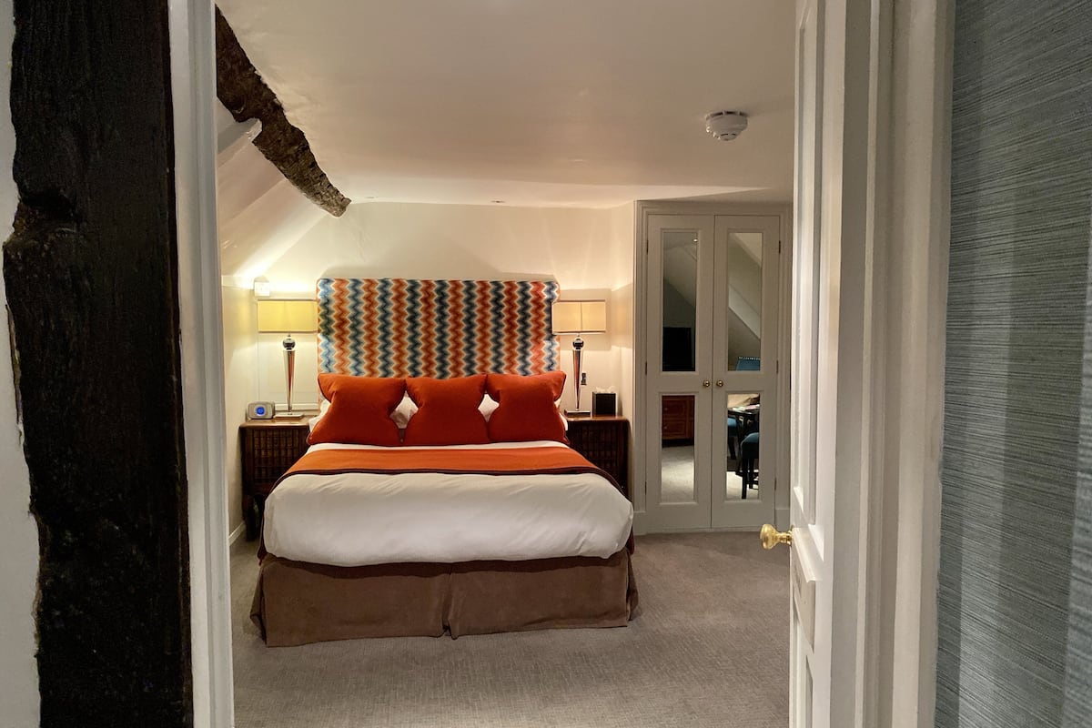 A bedroom with a large bed, a nightstand, a lamp, and a mirror.