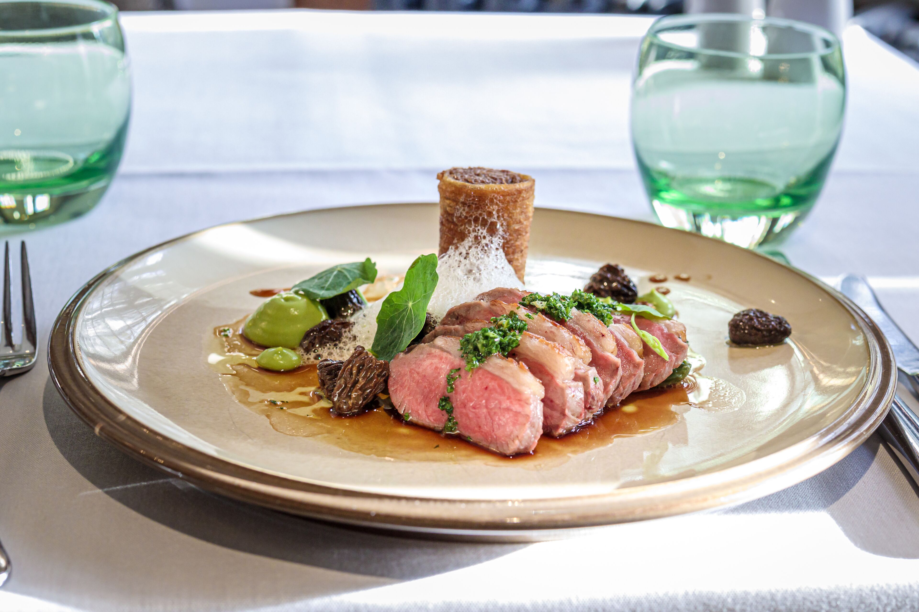 A plate of food with a bone, meat, and greens on a table with a white tablecloth.