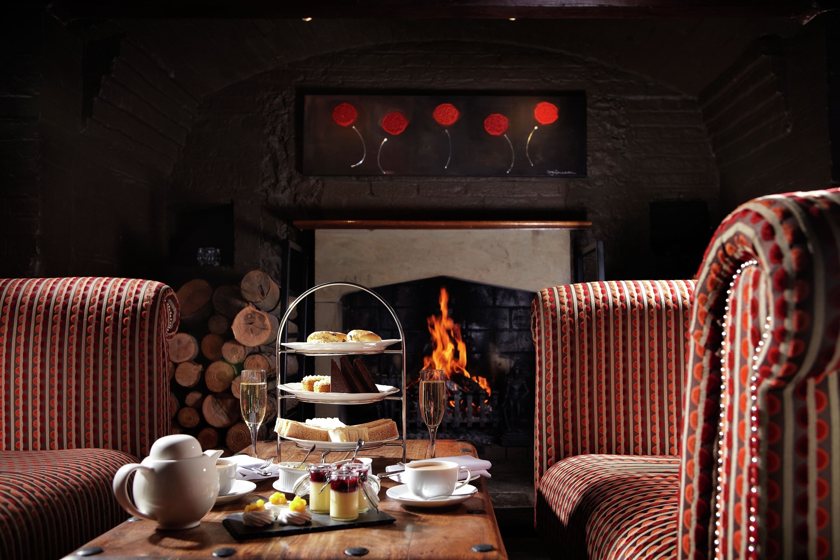 A cozy room with a fireplace, a three-tiered tea service, and striped upholstered chairs.
