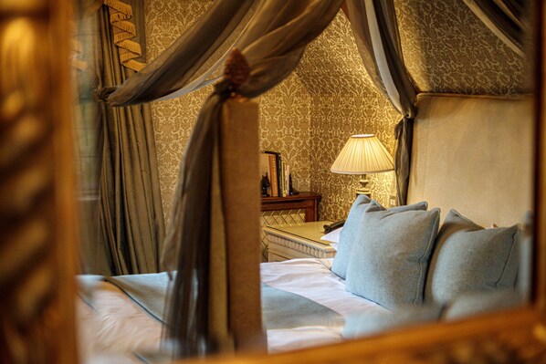 A bed with a canopy, a nightstand with a lamp, and a patterned wallpaper. - Langshott Manor (Horley)