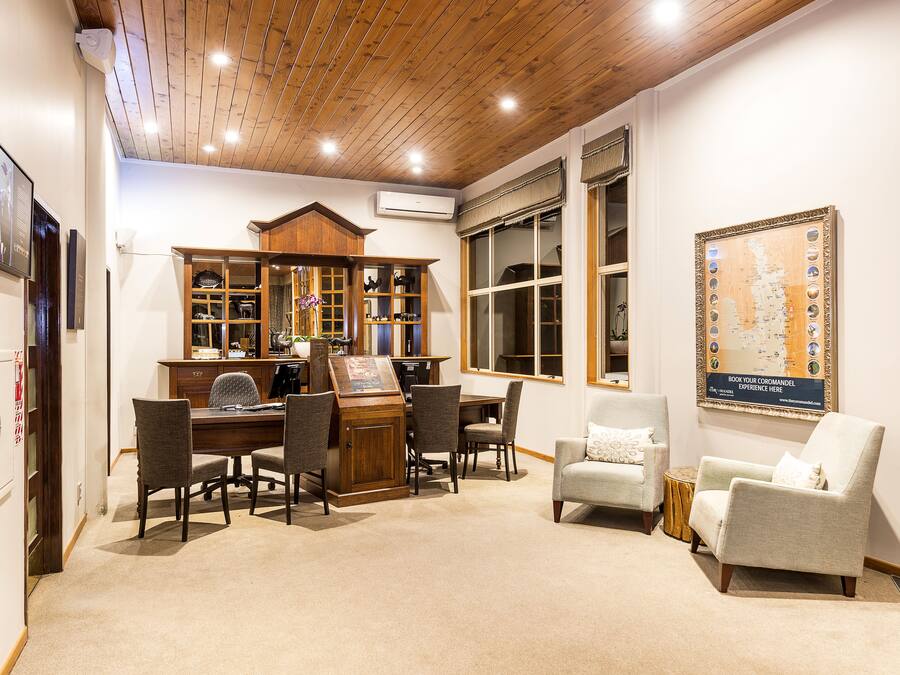 Um quarto com teto de madeira, uma escrivaninha com cadeiras, uma estante de livros, um sofá e um mapa na parede.