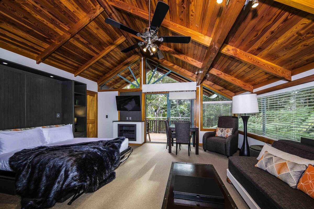 Una habitación amplia con cama, sofá, mesa de centro, televisor y ventilador de techo.
