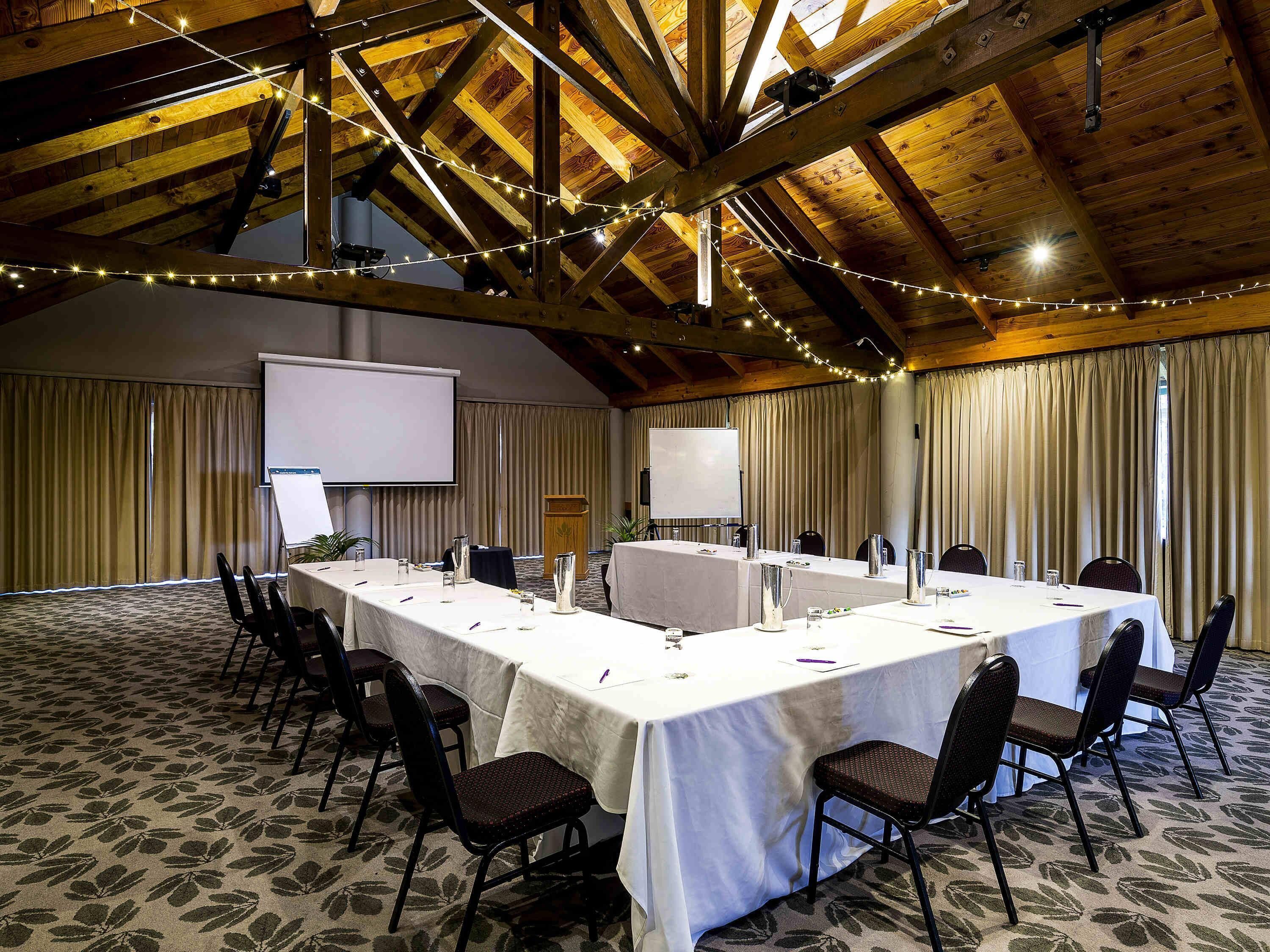 A conference room with a long table, chairs, a projector screen, and string lights.