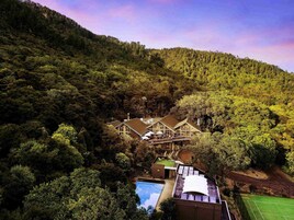 Una amplia casa rodeada de un bosque frondoso, con piscina y cancha de tenis a la vista.